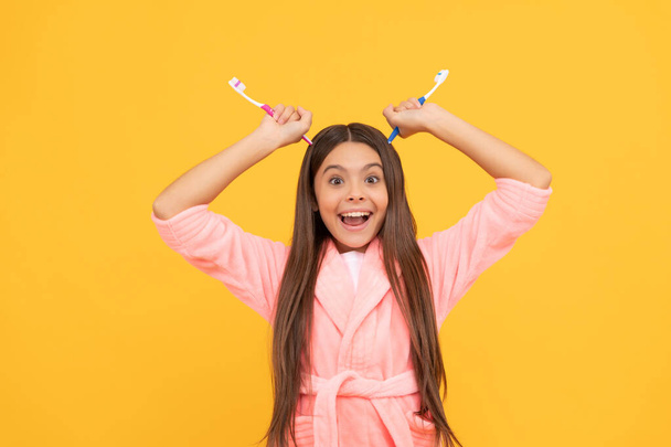 funny happy teen girl in home terry bathrobe hold toothbrush as devils horns, daily routine. - Photo, Image