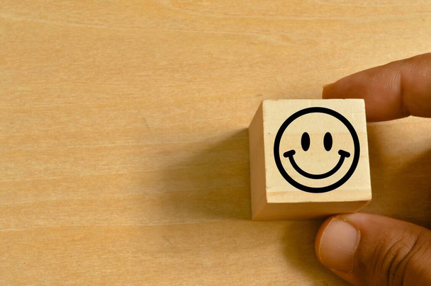 Człowiek ręka trzyma drewniany blok z uśmiechem szczęśliwy emocje twarzy na drewnianym tle - Zdjęcie, obraz