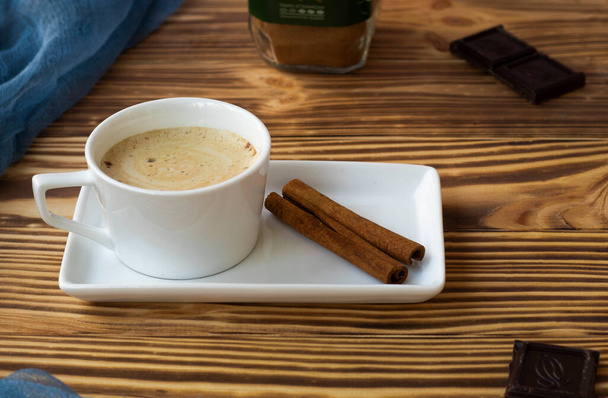 Bir fincan köpüklü latte, ahşap bir masada, kare bir tabağın üzerinde duruyor.. - Fotoğraf, Görsel