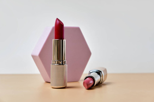 Two open lipsticks, an unbranded presentation of cosmetics on a light beige background with hexagon. - Фото, изображение