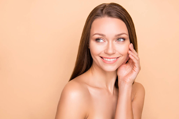 Profile photo of adorable lady arm touch cheek look empty space smile no clothing isolated on beige color background - Zdjęcie, obraz