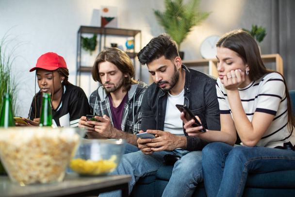 Multi ethnic friends using personal smartphones on couch - Foto, afbeelding