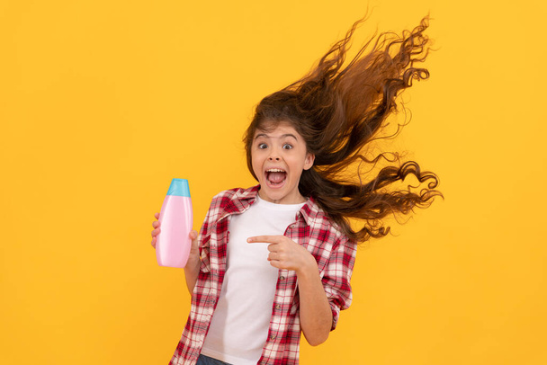 feliz adolescente chica con pelo largo rizado celebrar botella de champú, queratina. - Foto, Imagen