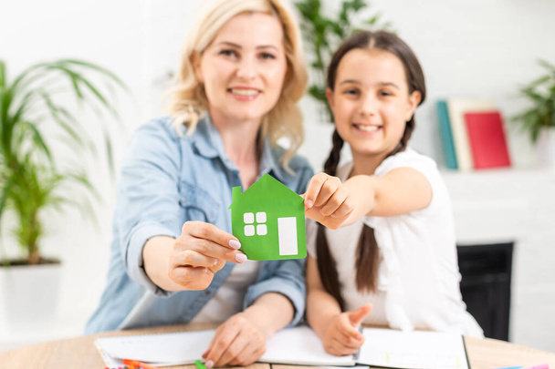 people, charity, family and home concept - close up of woman and girl holding green paper house cutout in cupped hands - Photo, Image