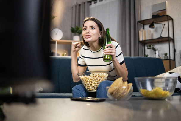 Woman with beer and snacks watching soccer match on TV - Photo, image