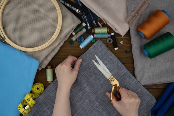 Vrouwelijke handen die kleding maken. Knippen en naaien aangepaste kleding. Schaar, naaiaccessoires, stoffen op een houten tafel. - Foto, afbeelding