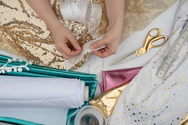 Female hands crafting clothes. Cut and sew customized garments. Gold scissors, threads, fabrics on a marble table. Sewing feminine, festive, glamorous, evening, wedding dresses, bridesmaids dress. - Photo, Image