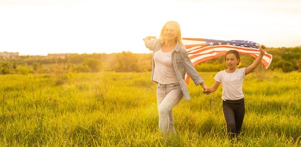 Patriotic holiday. Happy family, mother and her daughter child girl with American flag outdoors. USA celebrate 4th of July - Photo, Image