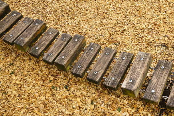 Een deel van het touw pad gemaakt van houten staven, bij elkaar gehouden door een metalen ketting.. De speeltuin is bedekt met houtsnippers. - Foto, afbeelding