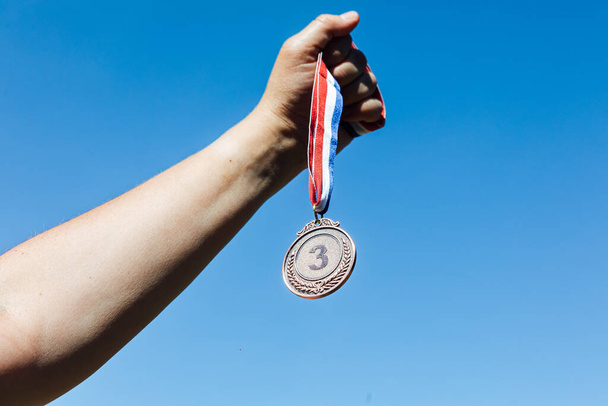 手は3位の銅メダルを持ち、空を背景にしている。勝利のコンセプト - 写真・画像