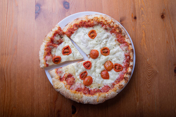 Overhead photo of a pizza with a cut slice on a wooden table - Photo, Image