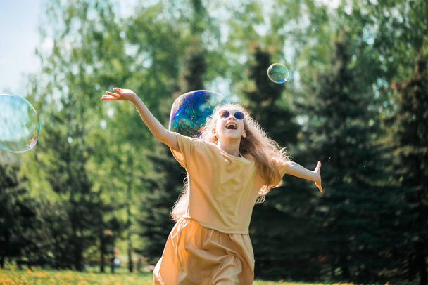 happy emotional sweet girl dancing and playing with soap bubbles enjoying a sunny day in the park. - Фото, зображення