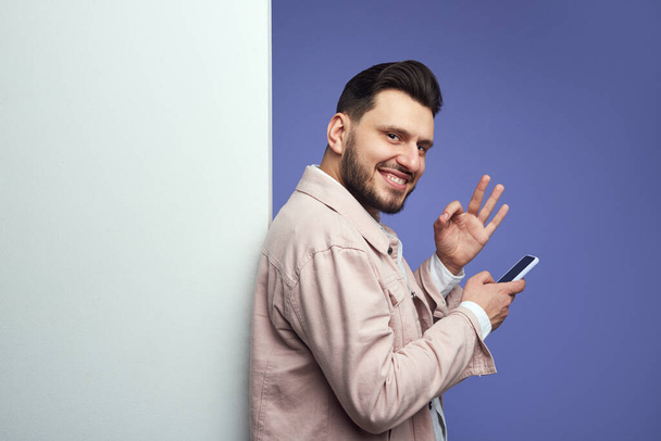 Человек, стоящий рядом с пустой белой стеной рекламного щита и показывающий жест в порядке - Фото, изображение