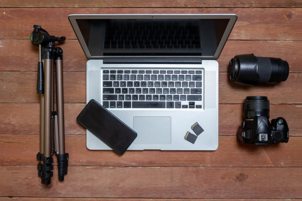верхний вид стола фотографа с фотографическим оборудованием, с камерой, объективом, ноутбуком и сотовым телефоном - Фото, изображение