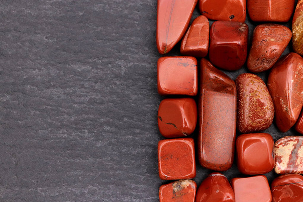 Red jasper heap jewel stones texture on half black stone background. Place for text. - 写真・画像