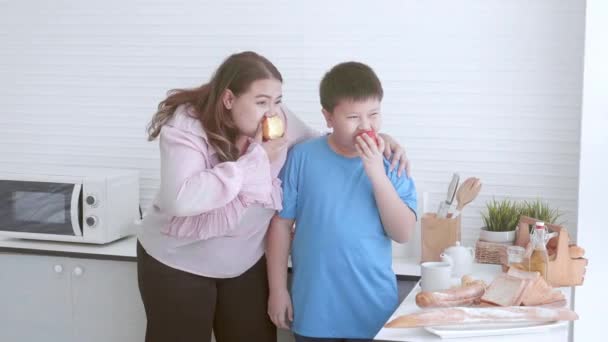 Genç Asyalı anne ve oğul evde mutfakta elma yiyorlar, sağlıklı meyveler yiyorlar, anne ve çocuk diyet yapıyor ve kilo veriyor, kadın ve çocuk aşırı kilolu ve besleyici, artı beden ölçüleri. - Video, Çekim