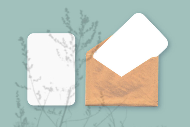 Mockup avec une superposition d'ombres végétales sur une enveloppe avec deux feuilles de papier blanc texturé sur un fond de table vert. Orientation horizontale - Photo, image