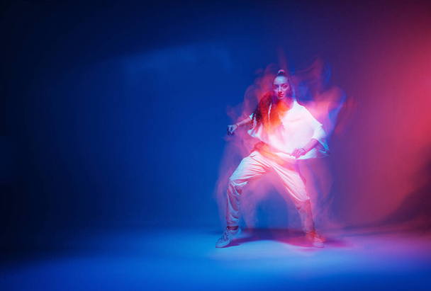 Stylish dancing modern girl moving in colorful neon studio light. Long exposure. Copy space - 写真・画像