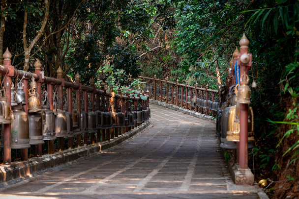 Chodník s kovovými bronzovými zvonky kolem a vedle něj v prostředí džungle, v chrámu Wat Phra That Doi Tung, provincie Chiang Rai, severně od Thajska. - Fotografie, Obrázek