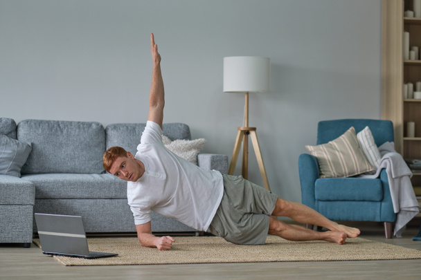 Zelfzorg tijdens het verblijf thuis. Fitness training, rekoefeningen online mannen thuis met laptop. man liggend op fitness mat online yoga lessen blanco laptop scherm - Foto, afbeelding