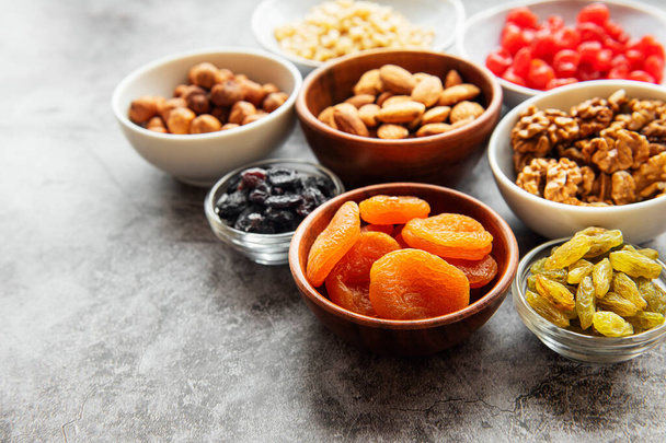 Bowls with various dried fruits and nuts on a gray concrete background - Photo, Image