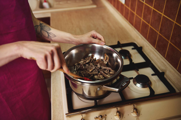 Closeup de confeiteiro Chocolatier segurando uma espátula de madeira e aquecimento e derretimento de chocolate em banho de água em um fogão na cozinha - Foto, Imagem