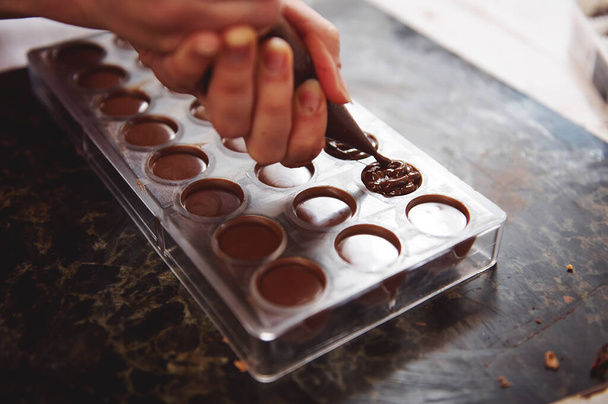 Pastelero relleno de moldes de chocolate vacíos con relleno para una mayor preparación de productos de chocolate hechos a mano de lujo. Primer plano. - Foto, imagen