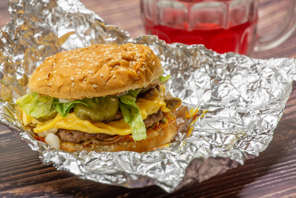 A closeup shot of a hamburger with foil on the table - 写真・画像
