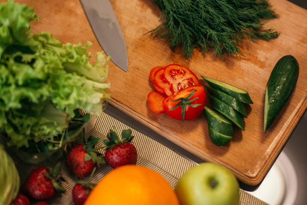 Zamknij strzał kuchnia czerwony pomidor ogórek sałatka zielony liść produkty owoce warzywa drewniane cięcia deska do siekania. Pani przygotowuje obiad śniadaniowy, gotować zdrowe jedzenie, copyspace dla wiadomości tekstowych. - Zdjęcie, obraz