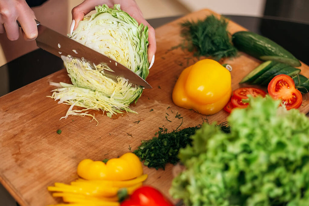 Close up shot woman standing kitchen hold hand cabbage products fruits vegetables wooden cutting board. Lady preparing breakfast lunch after training, want cook healthy food, copyspace. - Photo, Image