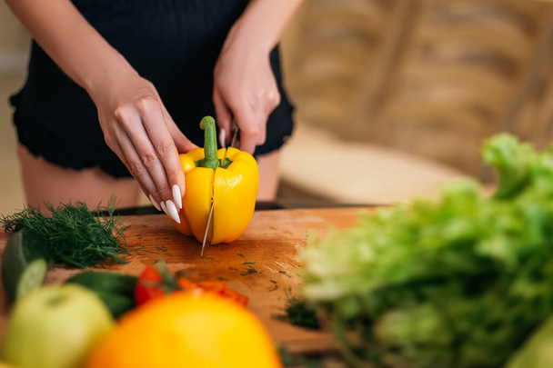 Close up shot woman standing kitchen hold hand yellow pepper products fruits vegetables wooden cutting board. Lady preparing breakfast lunch after training, want cook healthy food, copyspace. - Photo, Image