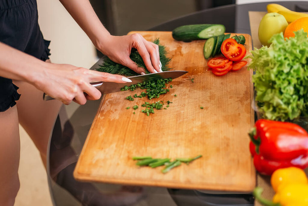 Close up shot woman standing kitchen chopping green salad dill plant products fruits and vegetables wooden cutting board. Lady preparing breakfast lunch after training, cook healthy food, copyspace. - Foto, immagini