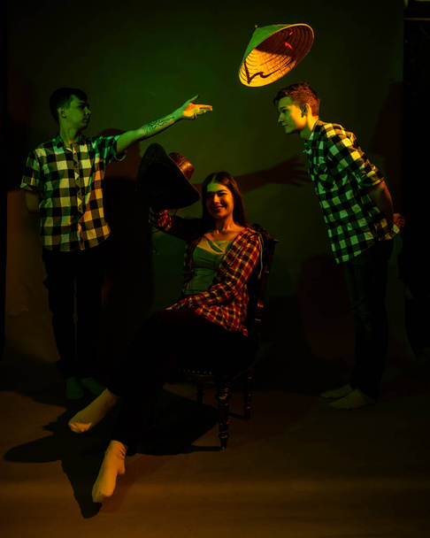 Two guys and a girl in plaid shirts in a studio with a multicolored light - Фото, зображення