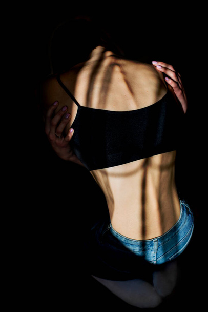 Een meisje met anorexia draaide zich om, ruggengraat en ribben zichtbaar. Getonen in koude tinten voor dramatisch effect. - Foto, afbeelding