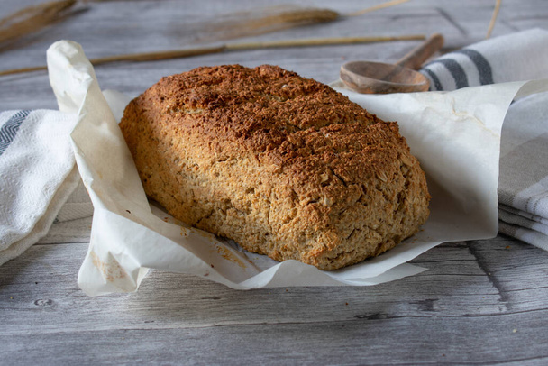 fresh and homemade baked gluten free oat bread with natural ingredients. Clean eating. Served on baking paper on rustic wooden table background. Closeup and isolated view.  - Photo, Image