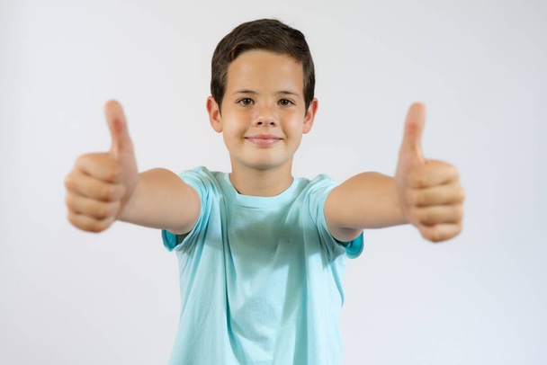 Cheerful smiling little boy standing over white background and showing thumbs up - Fotografie, Obrázek