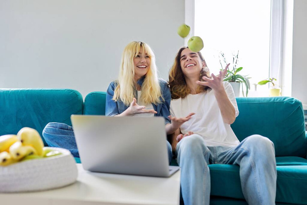 Laughing couple of teenagers having fun, sitting on couch, looking at laptop - Foto, Imagem