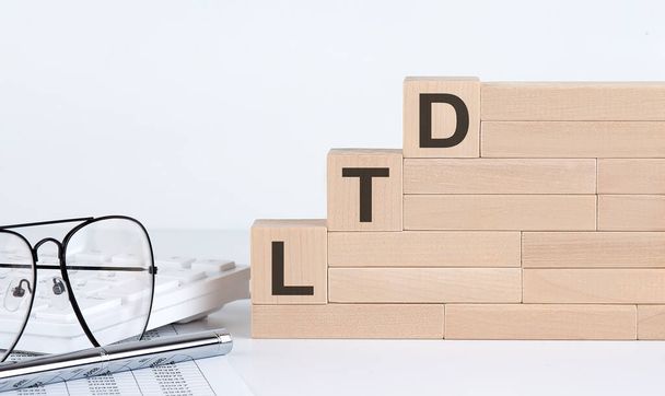 Три дерев'яні кубики з літерами LTD на білому столі з клавіатурою та окулярами
 - Фото, зображення
