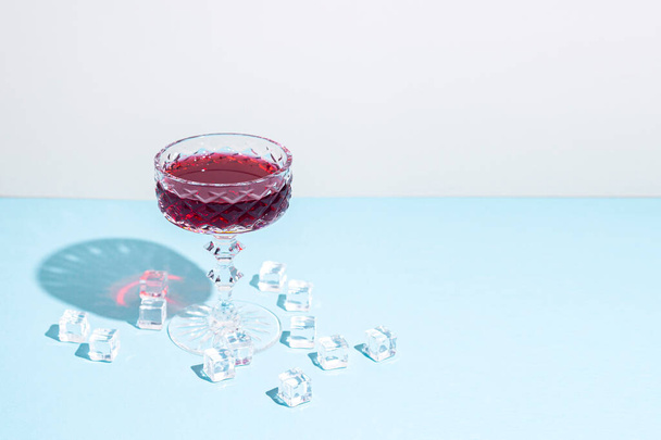 üveg vörösborral, jégkockák az asztalon, kék alapon. - Fotó, kép