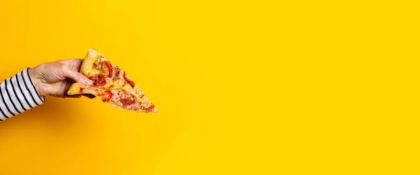 female hand holds a slice of fresh hot pizza on a yellow background. Banner. - Fotoğraf, Görsel