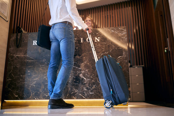 cropped image of young fit caucasian business man with laptop and luggage checking in hotel at reception - Foto, imagen