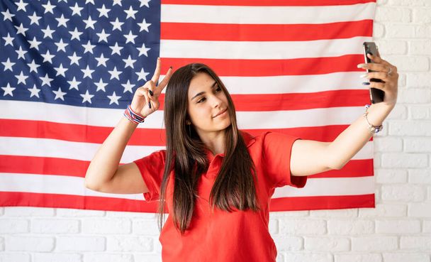 Ημέρα ανεξαρτησίας των ΗΠΑ. Χαρούμενη 4η Ιουλίου. Όμορφη γυναίκα που παίρνει μια selfie στο φόντο σημαία των ΗΠΑ - Φωτογραφία, εικόνα