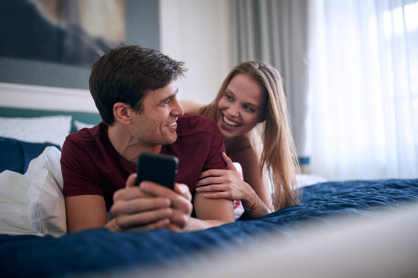 若い白人の大人のカップルはベッドに横になって笑って楽しんで楽しい時間を過ごしています. - 写真・画像