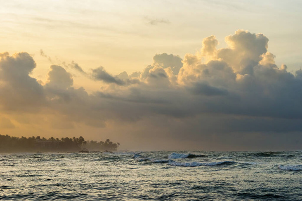 Σύννεφα ανατολή στη Σρι Λάνκα. Ινδική ακτή του ωκεανού το πρωί με φοίνικες σιλουέτες και κύματα που σπάνε. - Φωτογραφία, εικόνα