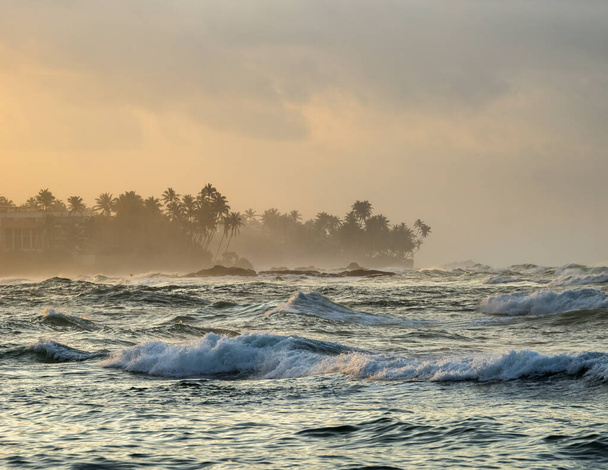 Paisaje marino matutino en Sri Lanka. Poderosas olas rompiendo en la orilla del océano Índico con siluetas de palmeras en el horizonte. - Foto, Imagen