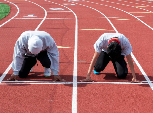 Elöl két középiskolás sprintert, akik készen állnak, hogy egymás ellen versenyezzenek az edzésen, egy közeli piros pályán.. - Fotó, kép