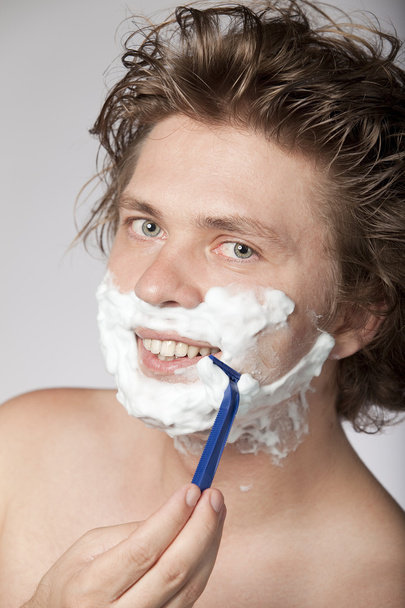 Attractive young man shaving with razor and smiling. High resolution image. See more in my portfolio - Foto, Bild