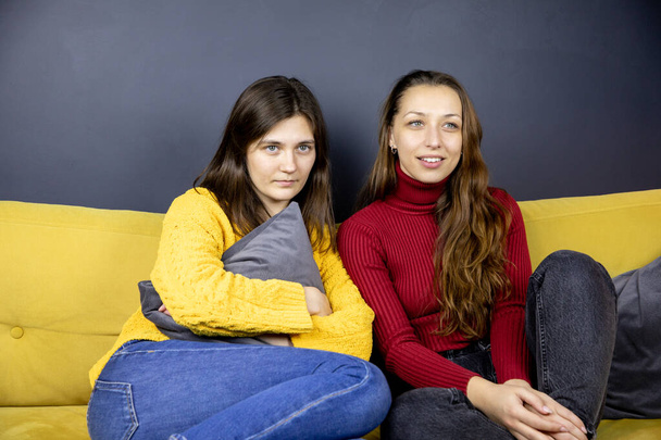 zwei ziemlich langhaarige brünette Mädchen sitzen auf dem Sofa und gucken zusammengekauert Fernsehen - Foto, Bild