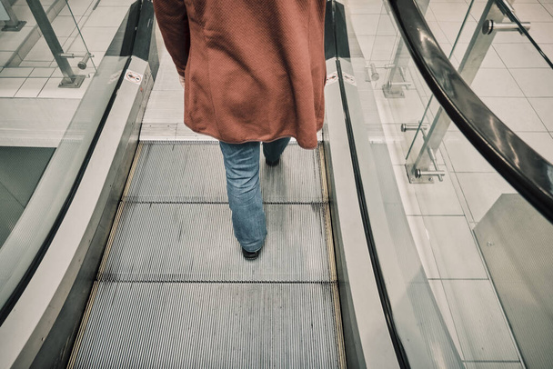 Kırmızı ceketli beyaz kadın alışveriş merkezinde demir bir yürüyen merdivende yere düşüyor. - Fotoğraf, Görsel