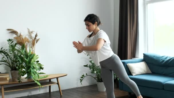 Mujer en ropa deportiva balanceándose en una pierna mientras repite asanas. Mujer de bajo ángulo haciendo yoga en casa durante el encierro. Formación a distancia - Metraje, vídeo